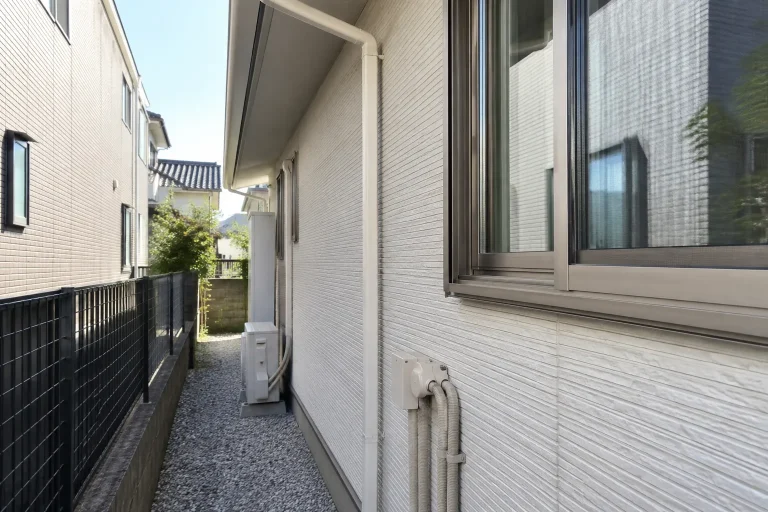 窓・雨樋・外壁に付く配管と敷地側の通路を写す。外壁が厚くなった場合の取り合い確認を連想できる構図。