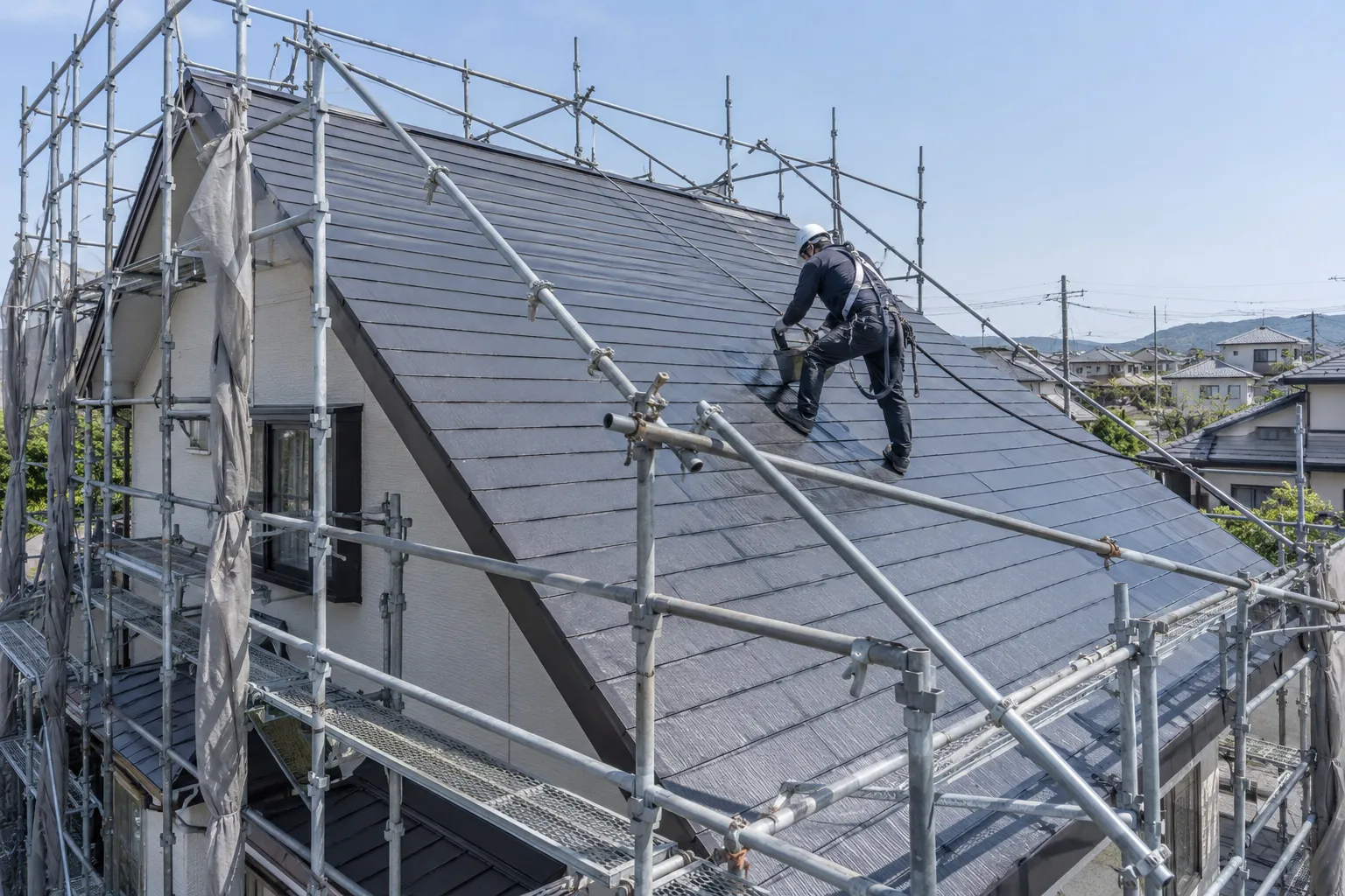 足場を設けた急勾配の屋根を塗装する作業員